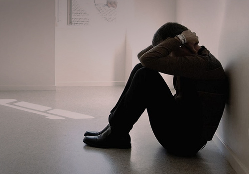Мужчина сидит в пустой комнате, опустив голову